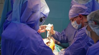 Geniş cerrahi ekip diz ameliyatı yapıyor. Koruyucu giysiler içindeki doktorlar metal tıbbi aletleri tutuyor..