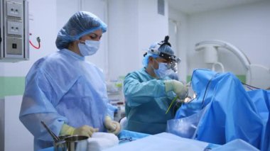 Hemşire aletleri hastada oturan doktora verir. Kafa üstü gözlüklü Otolaryngologist burun ameliyatı yapar..
