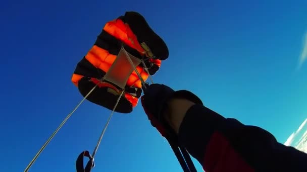 白い雲の間で空中に鳴る 黒とオレンジのパラシュートのストラップを保持する手 — ストック動画
