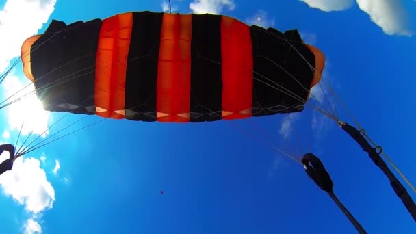 黒とオレンジのパラシュートのカポーラの下 極端なスポーツマンが土地に降り立った 青い空の下に美しい絵画の景色 — ストック動画