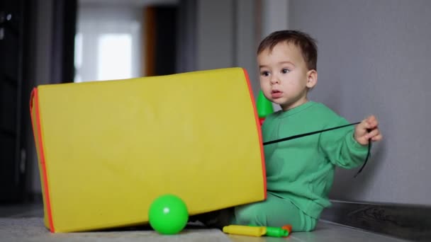 Кавказька Дитина Сидить Біля Жовтого Іграшкового Ящика Граючи Чорним Шнуром — стокове відео