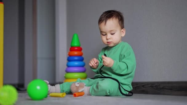 Sevimli Çocuk Elinde Ayakkabı Bağcığıyla Yerde Oturuyor Ağzına Alıyor Oyuncaklar — Stok video
