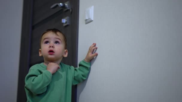 可爱的小男孩抱着墙站在昏暗的房间里 好奇的孩子打开开关 打开灯 — 图库视频影像