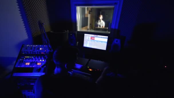 在黑暗的专业音乐录音室工作的音频工程师 歌手在隔壁窗户后面表演 — 图库视频影像