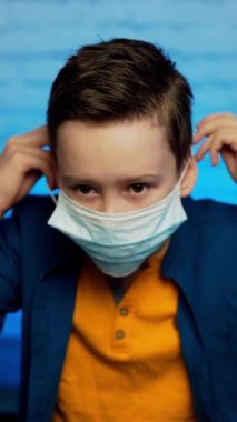 Virüslerden, salgınlardan, hava kirliliğinden ve tehlikeli parçacıklardan korunmak için tıbbi maske takan genç bir çocuk. Koronavirüsü durdurun. Dikey video
