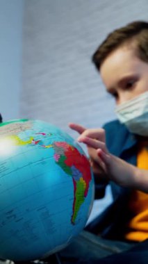 Dünyaya bakan bir çocuk virüsün tüm dünyaya yayıldığını öğreniyor. Tıbbi maske takan çocuk. COVID-19 salgını konsepti. Dikey video