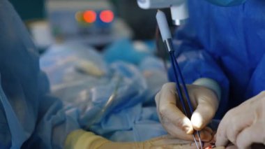 Tam bir estetik cerrah işi. Modern hastanede göğüs implantasyonu ameliyatı. Doktor elektrikli cihaz kullanıyor. Doktor için hastanın derisini tutan hemşire..