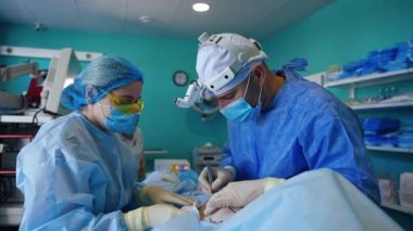 Erkek cerrah neşteri kullanarak hastanın göğsünün altını dikkatlice keser. Hemşire süngerle temizliyor. Modern hastanede göğüs implantasyon prosedürü.
