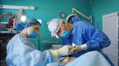 Kadın hemşire, metal bir aletle kaldırılmış bir hastanın derisini tutuyor. Cerrah göğüs boşluğuna implant için gerekli aletleri yerleştirir..