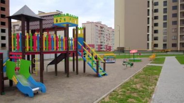Merdivenleri, slaytları ve tahtaları olan güzel renkli çocuk parkı. Arkaplanda çok katlı bina inşa ediliyor.