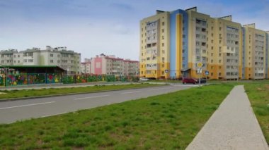Yeni inşa edilmiş çok katlı binalarla güzel, rahat bir yerleşim yeri. Arabalar yol kenarında hareket ediyor. Yeşil çimenli bir ev.