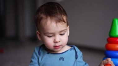 Mavi tişörtlü şirin beyaz çocuk oyuncaklarla oynuyor. Küçük bir erkek bebeğin bir oyuna odaklanmış portresi. Kapatın. Bulanık arkaplan.