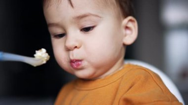 Kaşıkla beslenen sevimli bir bebeğin portresi. Anne oğluna içi süzme peynir dolu bir kaşık veriyor ve o da bunu isteyerek alıyor. Kapat..
