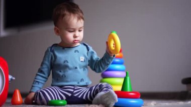 Tatlı çocuk piramit halkalarını temelden kaldırıyor. Kafkasyalı çocuk yüzüğü fırlattı ve geri almak için mutlu bir şekilde onu takip etti..