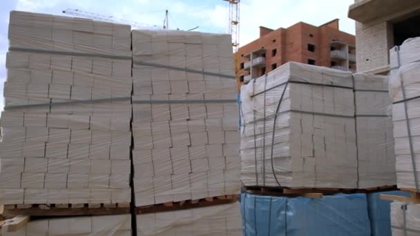 プラスチックで覆われた白い煉瓦の山 屋外の建設現場 バックドロップでのフラットの未完成のブロック — ストック動画