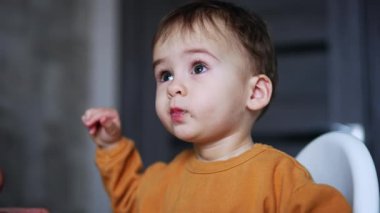 Turuncu gömlekli çocuk yulaf lapası yiyor. Sevimli çocuk annesinden bir kaşık alıyor. Kapatın. Bulanık arkaplan.
