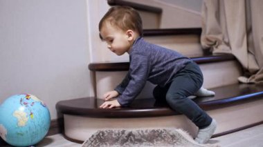 Evdeki merdivenlerde oturan tatlı bir erkek bebek. Tatlı çocuk, oyuncağı yerden almaya çalışırken elini uzatır..