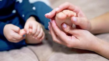 Annemin elleri bebek ayağını tutuyor ve okşuyor. Annem oğluyla evde vakit geçiriyor. Kapatın. Bulanık arkaplan.