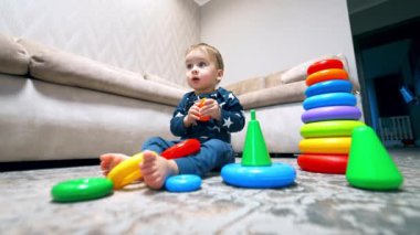 Kafkasyalı çocuk yerde parlak piramitlerle oynuyordu. Evde bir erkek bebek için oyun zamanı. Düşük açı görünümü.