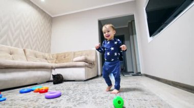 Gülümseyen mutlu çocuk odanın önünden geçiyor. Çocuk televizyonu açmaya çalışırken duvarda asılı duruyor. Düşük açı görünümü.