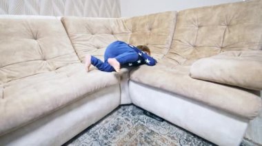 Mutlu küçük bebek kanepeye neşeyle tırmanıyor. Sevimli aktif çocuk salonda tatlı tatlı gülümsüyor..