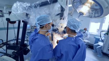 Cerrahların arkası mikroskop önünde dürbüne bakıyor. Doktorlar aletleri yavaşça hastayı ameliyat ediyor..