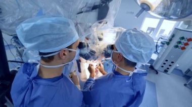 Nöroşirürji ekibi modern hastanede ameliyatı gerçekleştiriyor. Ana cerrah gelişmiş mikroskopla ameliyat alanına bakıyor. Üst görünüm.