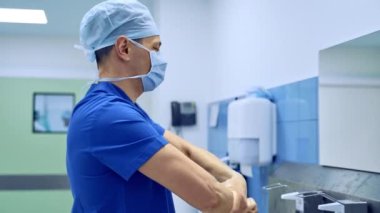 Cerrah ellerine bir sürü antiseptik uygular. Profesyonel, kollarını dirseğine kadar sterilite etmek için antiseptik sıvıyla kapatmış..