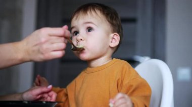 Kaşıkla yemek yiyen güzel beyaz çocuk. İyi çocuk evde yemek yiyor. Kapatın. Bulanık arkaplan.