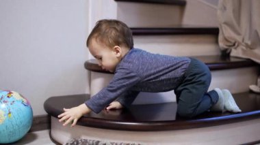 Kafkasyalı erkek bebek merdivenlerde dördünün üzerinde duruyor. Sevimli çocuk oyuncakla oynuyor, yere düşürüyor..