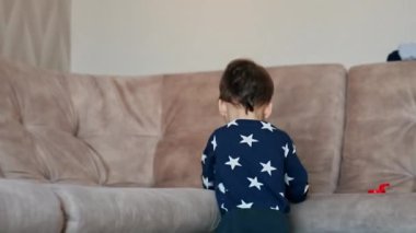 Bebek evde aktif zaman geçiriyor. Güzel çocuk kanepenin yanındaki odada bir oyuncakla dolaşıyor..