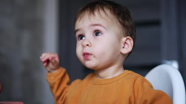 小孩穿着橙色衬衫吃粥 可爱的孩子从他母亲那里接过一只勺子 靠近点模糊的背景 — 图库视频影像