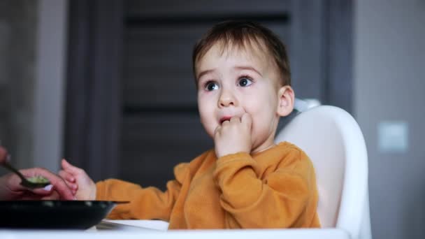 甜甜的孩子坐在白色的喂食椅上 会得到食物 有爱心的妈妈给儿子喝汤 靠近点模糊的背景 — 图库视频影像