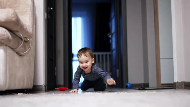 快乐兴奋的蹒跚学步的男孩快速地爬到地板上 婴儿停下来回头看 然后抱着沙发站了起来 — 图库视频影像