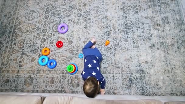 ソファーの下にたどり着こうとする赤ん坊の少年 子供は屋内で床で遊んでいる トップビューの視点 — ストック動画