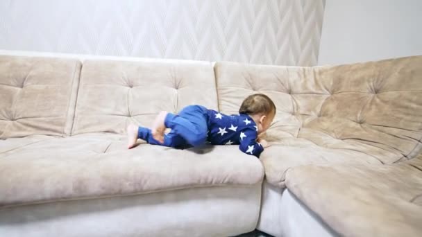 アクティブな白人の子供は大きなソファーでクロールします 自宅で楽しい青い服を着ている赤ちゃん — ストック動画