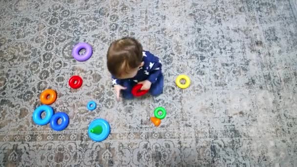 婴儿收集金字塔明亮的戒指 黑头发的孩子坐在地板上玩玩具 顶部视图 — 图库视频影像