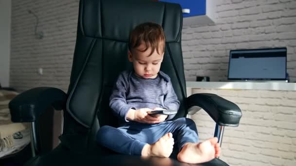 Uroczy Biały Dzieciak Siedzący Czarnym Fotelu Biurowym Trzymający Pilota Mały — Wideo stockowe