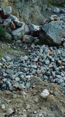 Yürüyüş yapan adam taş patikadan geçip kayalık bir yere geliyor. Dağlarda doğa yürüyüşü yapan bir turistin hava görüntüsü. Dikey video