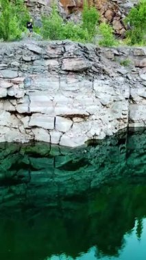 Rocky cliff yeşil suya ve yaz kıyafetleri içindeki turistlere yansıyor. Dağlarda doğa manzarası var. Kamera altta hareket ediyor. Dikey video