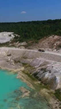 Açık çukur madenciliğinin muhteşem manzarası. Yığınla killi kamyon tepe boyunca gidiyor. Yeşil orman arka planı. Dikey video
