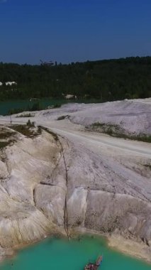 Şimdiki Kaolin madeninde yüklü bir kamyon yol boyunca ilerliyor. Beyaz tepe zemin, mavi su ve temiz gökyüzü. Arkaplanda yeşil ağaçlar var. Dikey video