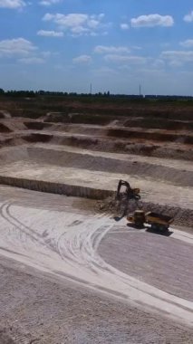 Kaolin taş ocağında düz zemin. Kazı makinesi kaya oluşumlarını kazıyor. Minerallerle yüklenen kamyon yaklaşıyor. Dikey video