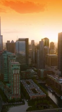 Günbatımının altın ışığında modern Chicago 'nun muhteşem mimarisi. Turuncu gökyüzünün arkaplanındaki güzel binaların arasında Chicago Nehri manzarası. Dikey video