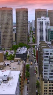 Modern binalar arasında sokaktan geçen geniş bir yol. Chicago 'nun gelecekteki mimarisi pembe gökyüzünün arka planında. Dikey video