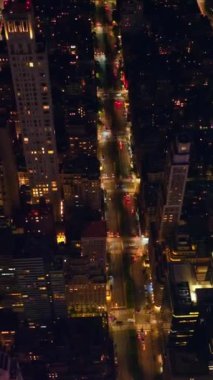 Gece vakti New York 'un parlak sokakları. İnsansız hava aracı ışıklarla dolu metropolün üzerinde uçuyor. Üst Manzara. Dikey video