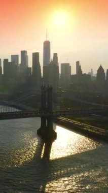 Gün batımında muhteşem New York 'un gri siluetleri. İnsansız hava aracı görüntüleri Doğu Nehri üzerindeki çarpıcı köprülere yavaşça yaklaşıyor. Arkaplanda pembe gökyüzü. Dikey video