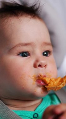 Bebek beslenirken dramatik bir yüz ifadesi takınıyor. Anne kaşığı oğlunun ağzına doğru itiyor. Dikey video