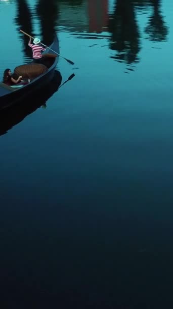 一个女人和一个吊船在晚河上漂流 戴着白帽和条纹衬衫的男人载着优雅的女人与灯笼在船上 快速的空中观察周围 垂直录像 — 图库视频影像