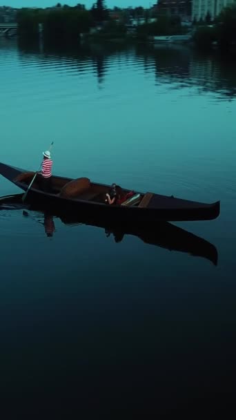 在空中看到一个戴着帽子的壮汉在夜间驾驶着船桨在河床上划船 女人坐在贡多拉 欣赏美丽的风景 垂直录像 — 图库视频影像